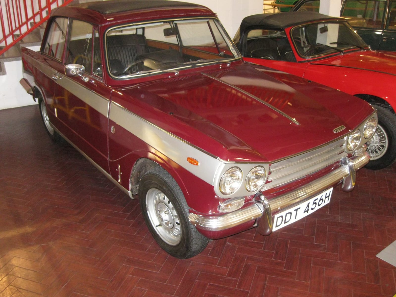A maroon Triumph Vitesse Mk2 saloon displayed in a museum, front three-quarter view, UK registration DDT 456B