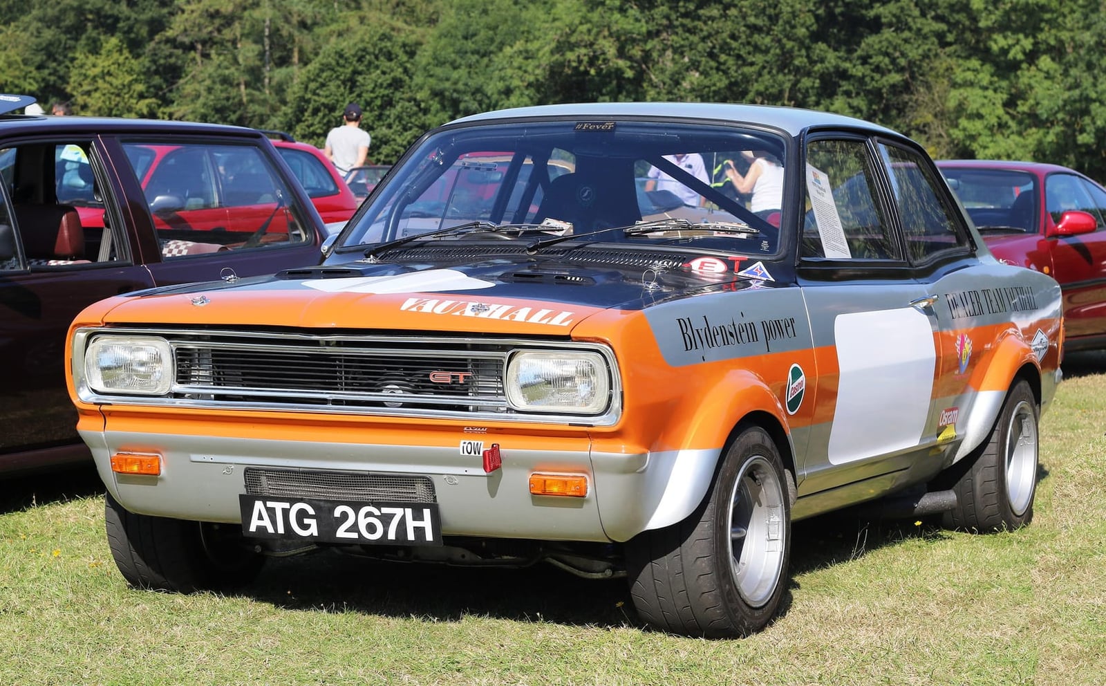 An orange and white Blydenstein-tuned Vauxhall Viva GT competition car on grass at a classic car show, UK registration ATG 267H